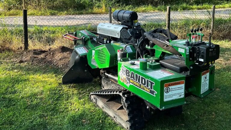 A green Bandit stump grinder parked on grass near a fence.